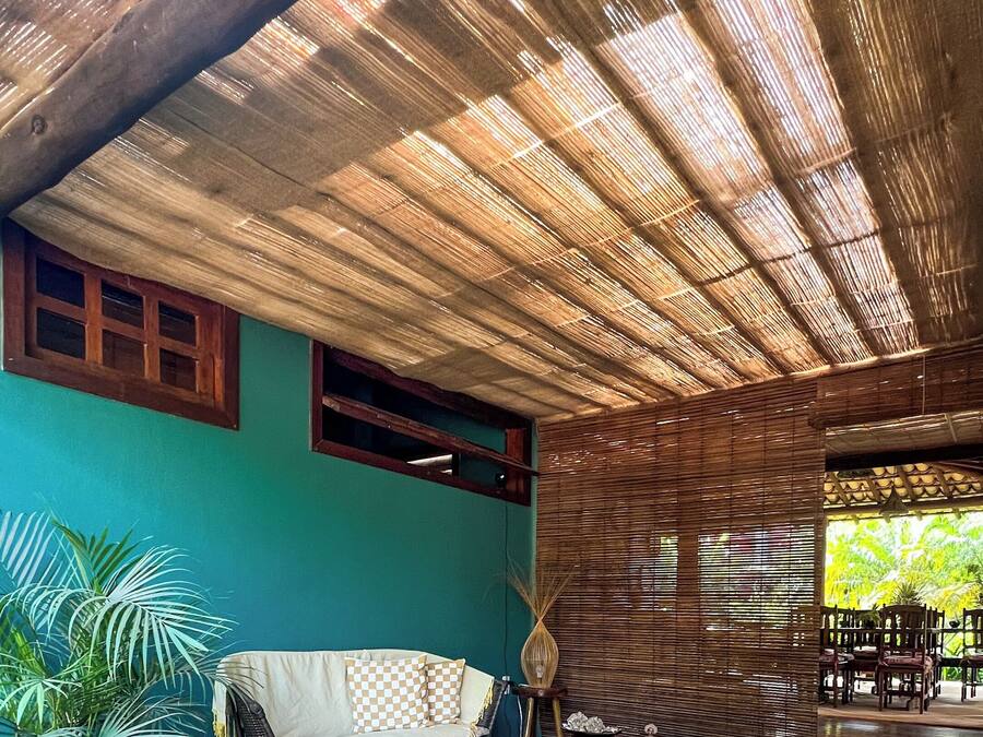 A covered outdoor seating area with a woven ceiling, a sofa, and a dining table.