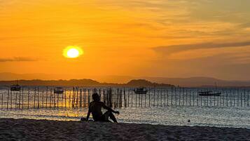 A sunset over a calm sea with a person sitting on the shore.
