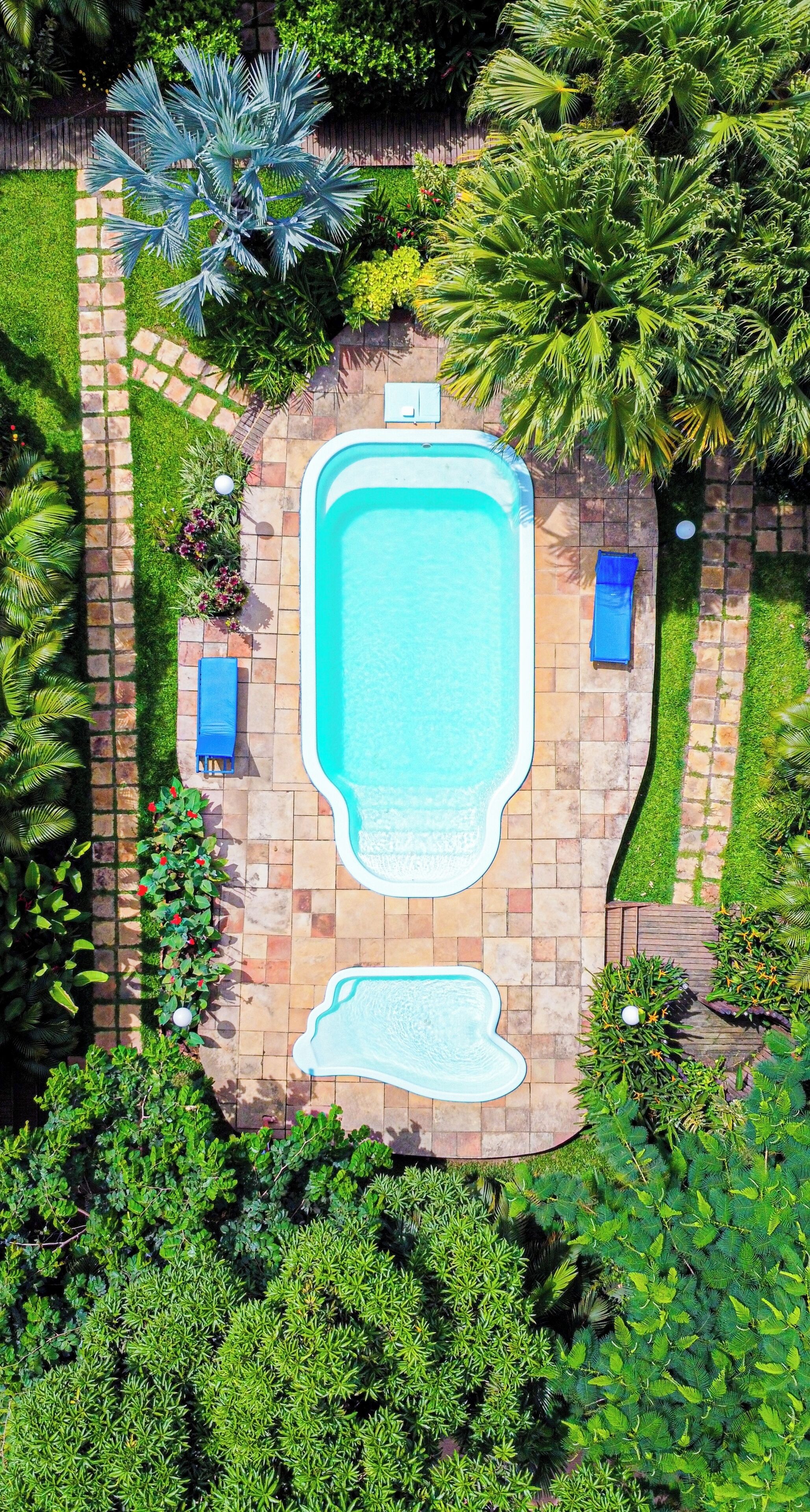Una piscina con due lettini e una piccola vasca idromassaggio, immersa nel verde e con un vialetto lastricato.