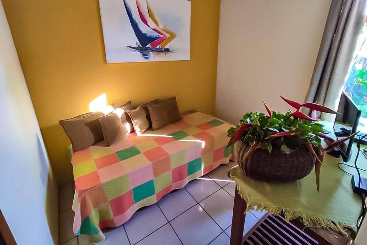 A room with a colorful checkered sofa, a painting of a sailboat, and a potted plant.
