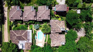 Vista aérea de un resort con varias cabañas y una piscina central, rodeado de abundante vegetación.