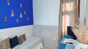 A room with a bed, a table with a laptop, a ceiling fan, and a wall with decorative items.