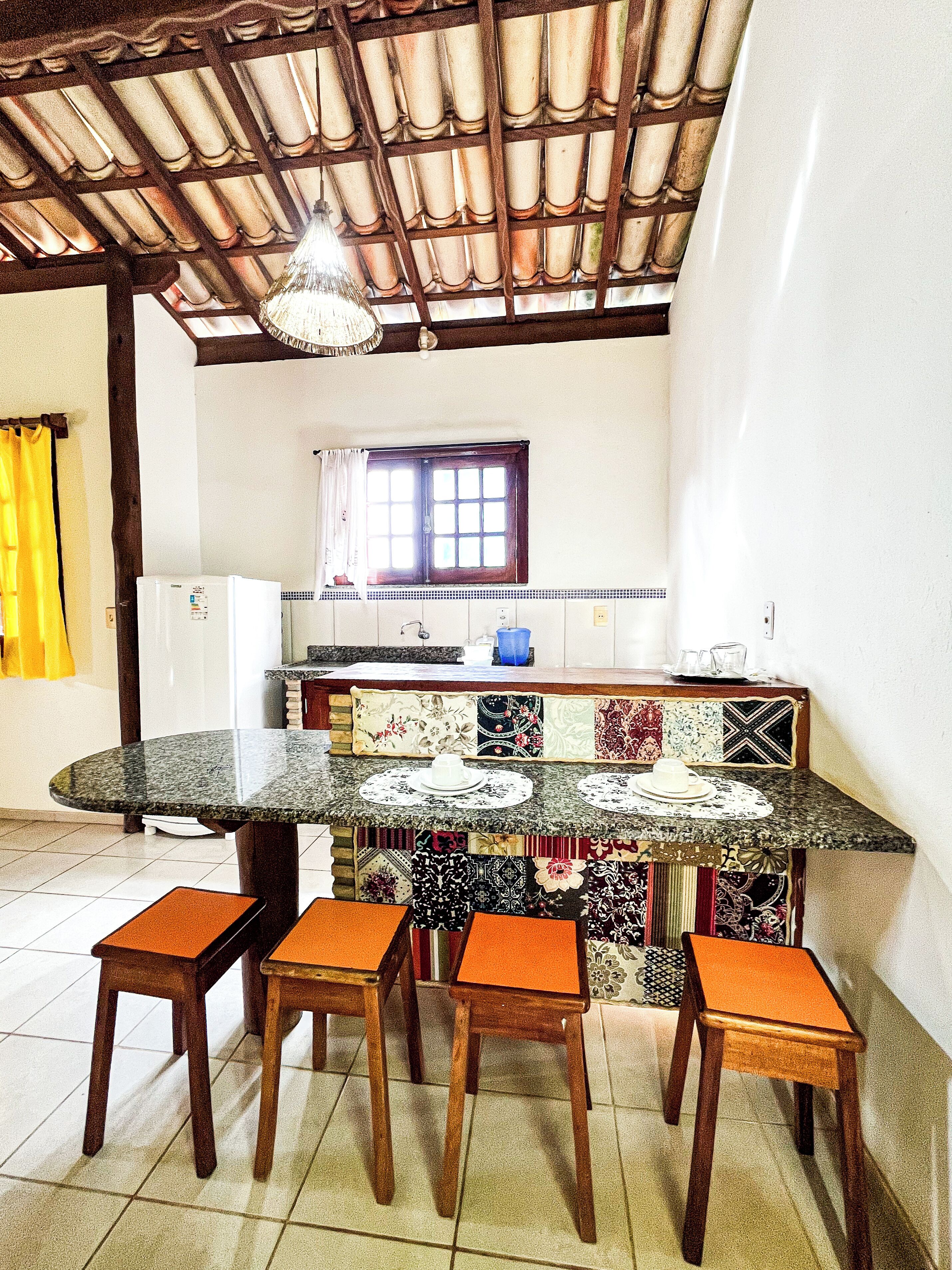 Una cocina con una isla central, taburetes de madera, un refrigerador y una ventana con cortinas.