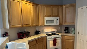 A compact kitchen with wooden cabinets, a white microwave, a stove, and a coffee maker. - Witter luxery home (Sacramento)