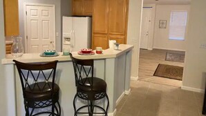 A kitchen with a white refrigerator, wooden cabinets, and two bar stools. - Witter luxery home (Sacramento)
