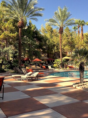 A pool area with lounge chairs and umbrellas, surrounded by palm trees.