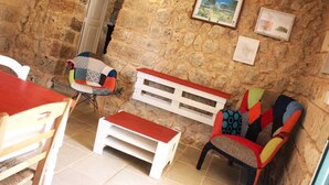 Una habitación acogedora con pared de piedra, un banco de madera, una silla colorida y una mesa blanca.