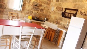 Una cocina con pared de piedra, una mesa de madera, sillas blancas, un refrigerador blanco y una olla amarilla sobre la encimera.