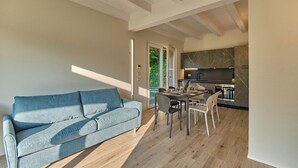 Un salon moderne avec un canapé, une table à manger et des chaises. On aperçoit au fond une cuisine avec des plans de travail en marbre foncé et une cuisinière.