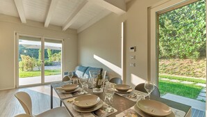 Un coin repas avec une table dressée pour quatre personnes, un canapé et une vue sur un jardin.