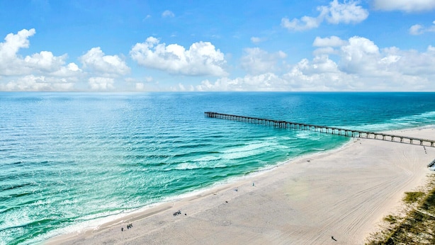 Ein Strand mit einer langen Pier, die sich ins Meer erstreckt, bewölktem Himmel und ruhigem Wasser.