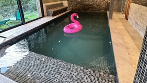 An indoor swimming pool with a pink flamingo float, stone walls, and a bench by the window.