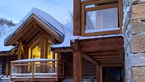A wooden cabin with a balcony, stone walls, and a snow-covered roof.