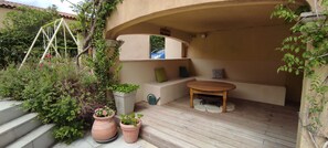 A cozy outdoor seating area with a wooden table and benches, surrounded by potted plants and a swing set. - Provence house with indoor swimming pool (Pélissanne)