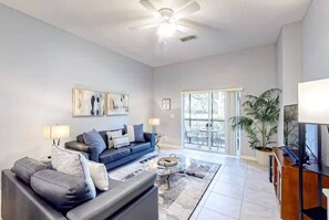 A spacious living room with a dark-colored sofa, a coffee table, and a ceiling fan. - Bahama Bay modern condo on ground floor (Davenport)