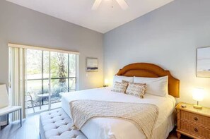 A bedroom with a large bed, a nightstand, a window with a view of the outdoors, and a chair by the window. - Bahama Bay modern condo on ground floor (Davenport)