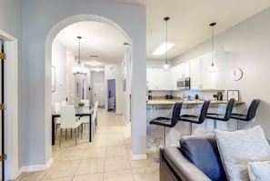 A modern kitchen with white cabinets, a dining area with white chairs, and a bar area with black bar stools. - Bahama Bay modern condo on ground floor (Davenport)