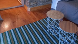 Ein gemütliches Schlafzimmer mit einer Steinstur und Holzboden, einem Bett mit Kissen, einem Nachttisch und einer Lampe.