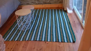 Ein kleiner, gemütlicher Raum mit Steinwand, einem Bett, einem Tisch und einem großen Fenster.