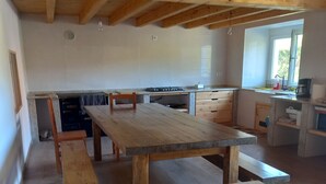 Eine geräumige Küche mit Holzbalken, einem großen Esstisch in der Mitte und eingebauten Schränken.