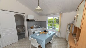 Une cuisine compacte avec une table à manger, des chaises blanches et une vue sur un jardin grâce à une grande fenêtre.