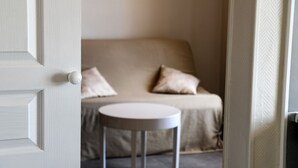 Une pièce avec un canapé beige, deux coussins et une petite table ronde.