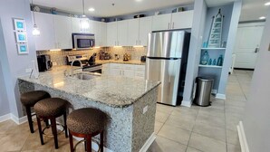 A modern kitchen with a granite island, stainless steel appliances, and a tiled backsplash. - Beachfront Bliss! 4th-Floor Condo 2BR/2BA Sleeps 8! Steps from the water! (Panama City Beach)