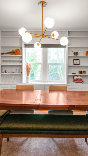 Uma área de refeições com mesa de madeira, bancos e um lustre moderno.