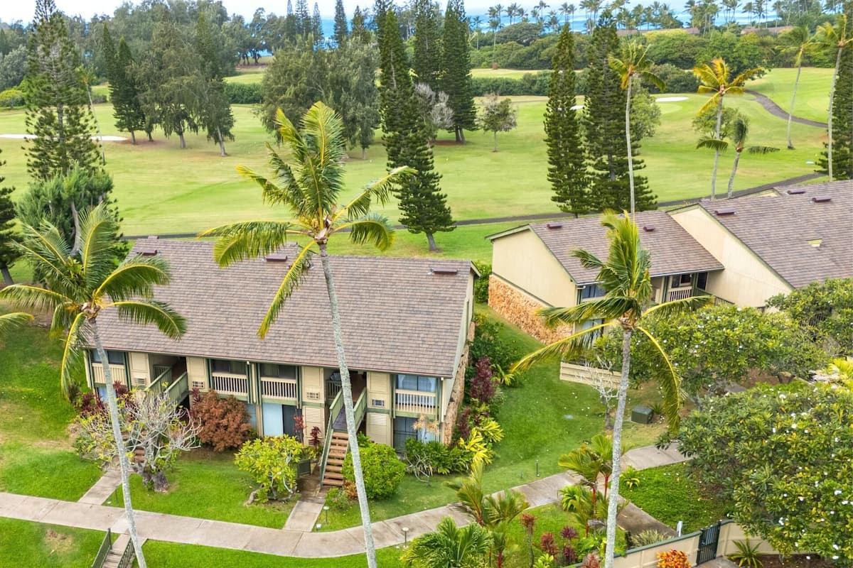A residential area with houses, palm trees, and a golf course in the background.