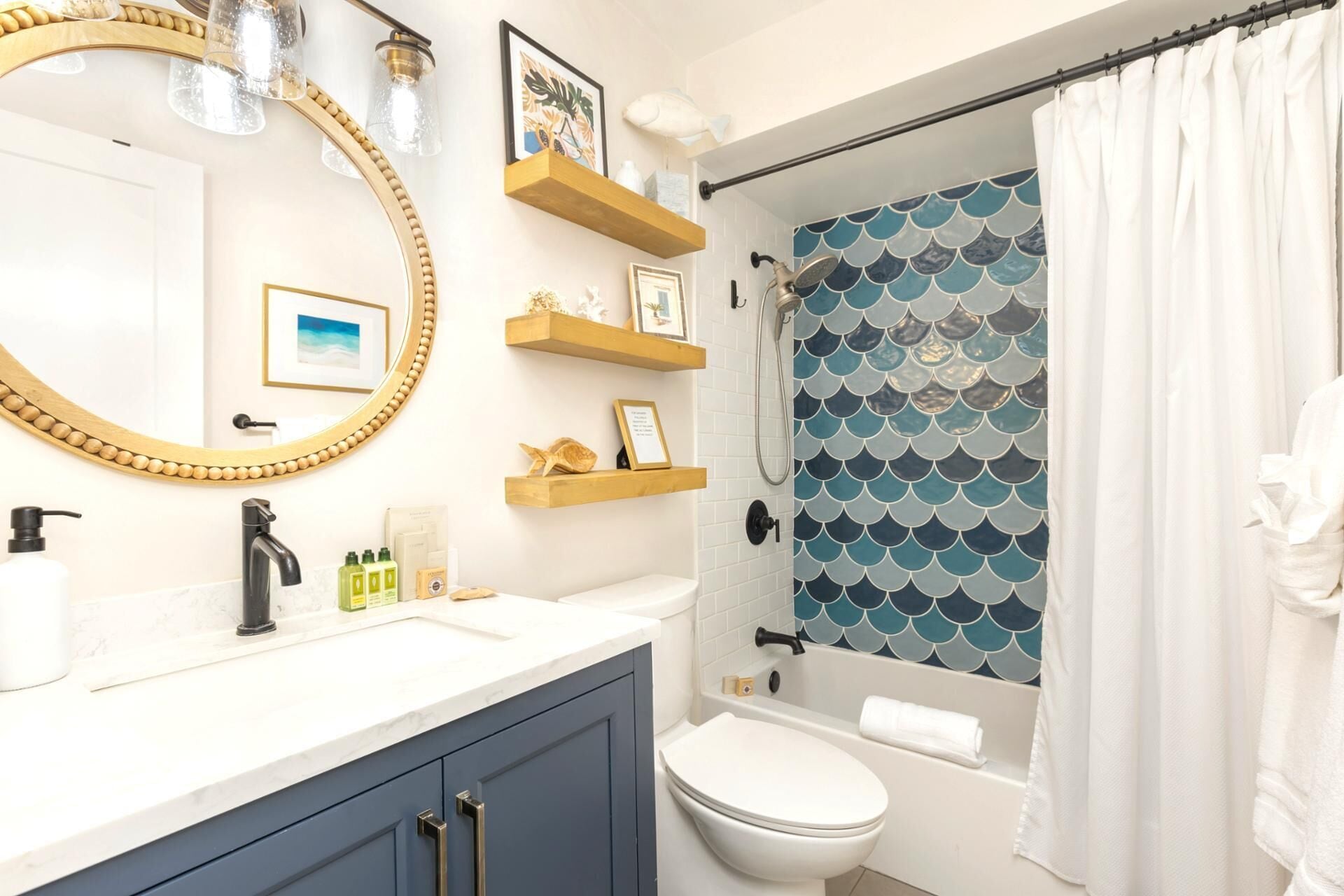 Une salle de bain avec un lavabo blanc, des toilettes, une baignoire et un rideau de douche orné d’un motif écaille bleu et blanc.
