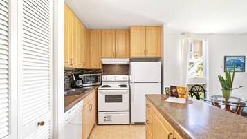 Une cuisine compacte avec des meubles en bois, un réfrigérateur blanc, une cuisinière et un four à micro-ondes. Une fenêtre donne sur un balcon.