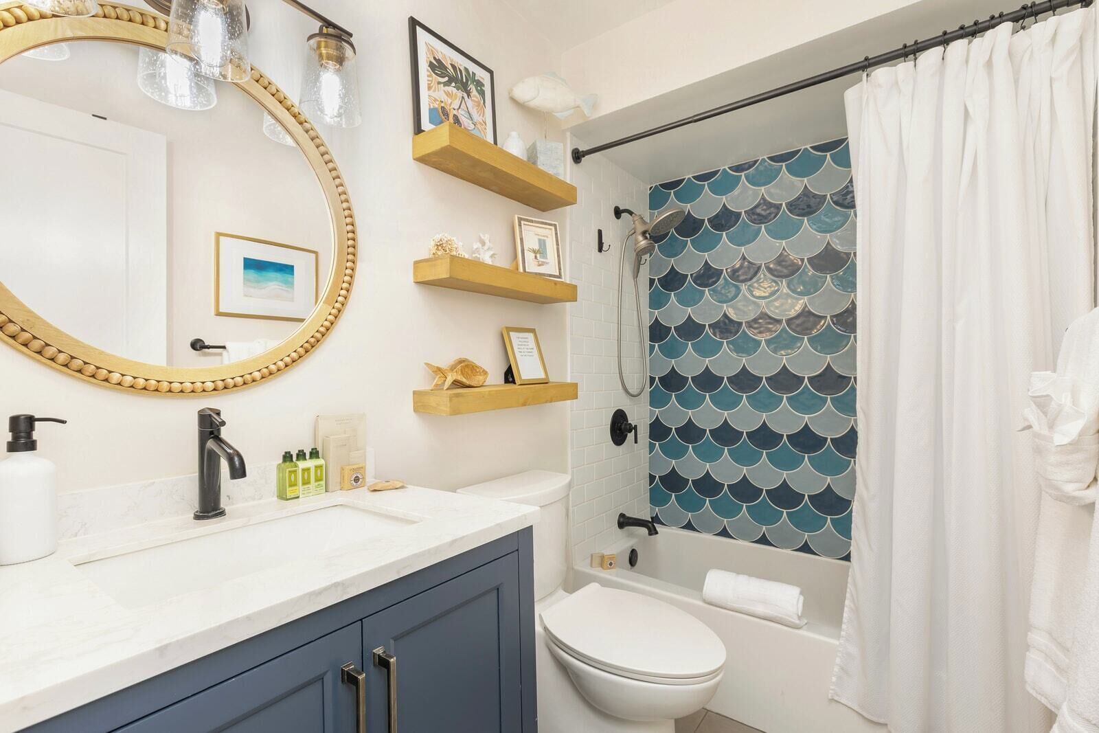 A bathroom with a white sink, a toilet, a shower with a blue tiled wall, and wooden shelves with toiletries.