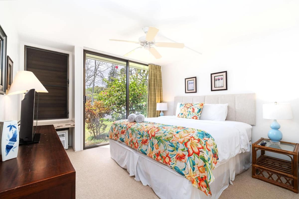 A bedroom with a bed, a ceiling fan, a window, and a view of the outdoors.