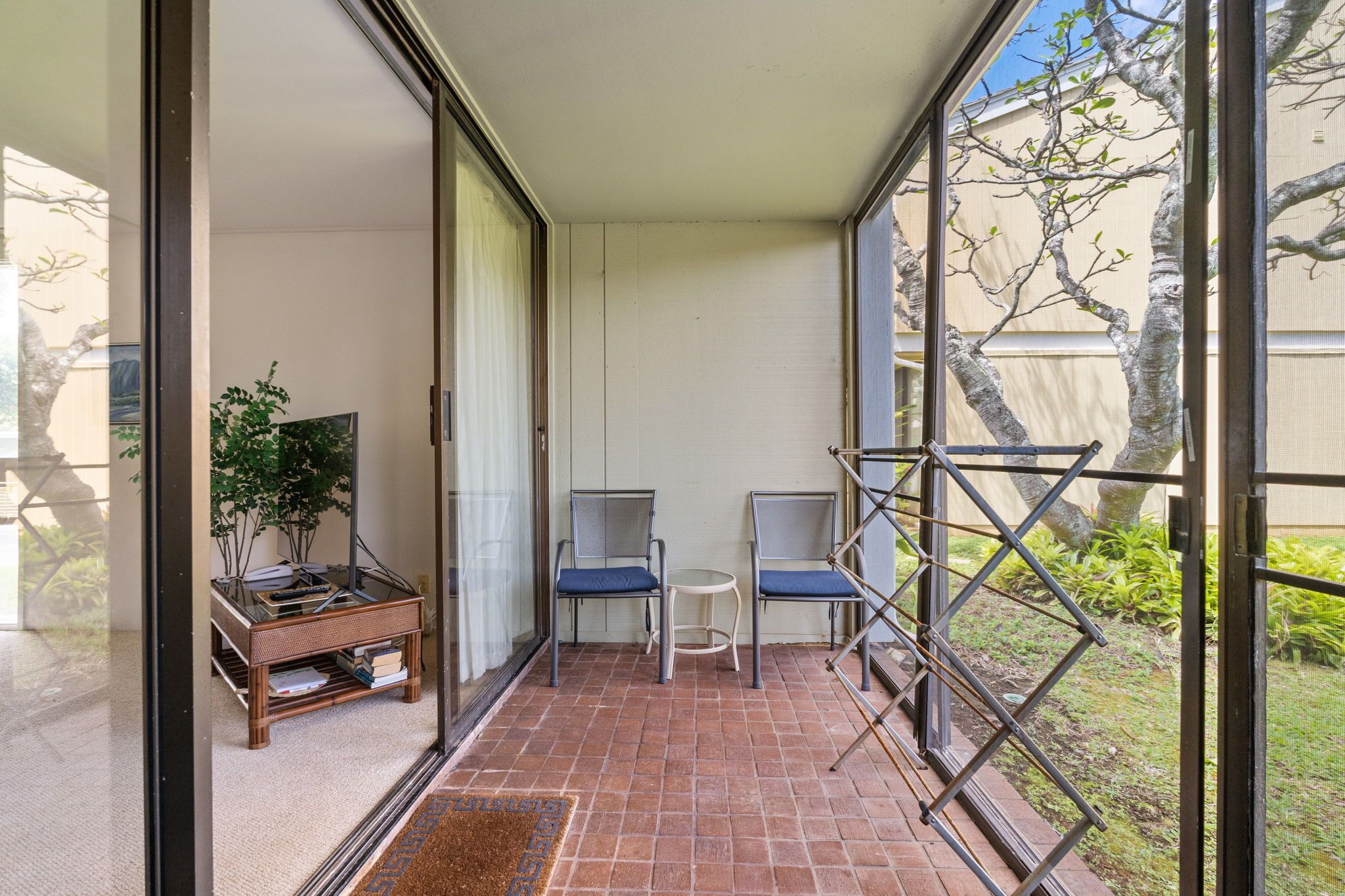 A balcony with a view of trees, two chairs, a small table, and a plant.