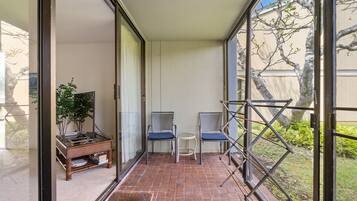 A balcony with a view of trees, two chairs, a small table, and a plant.