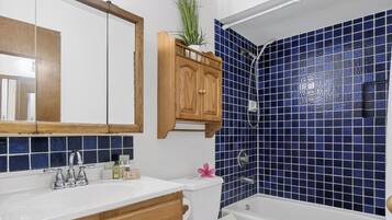 A bathroom with a white sink, wooden cabinets, a mirror, a shower with blue tiles, and a toilet.