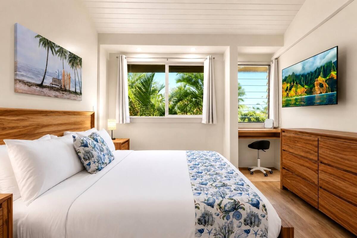 Ein Schlafzimmer mit Bett, Schreibtisch, Stuhl, Fernseher und einem Fenster mit Vorhängen.