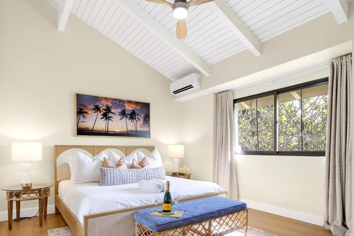 A bedroom with a bed, a nightstand, a lamp, a window with curtains, and a ceiling fan.