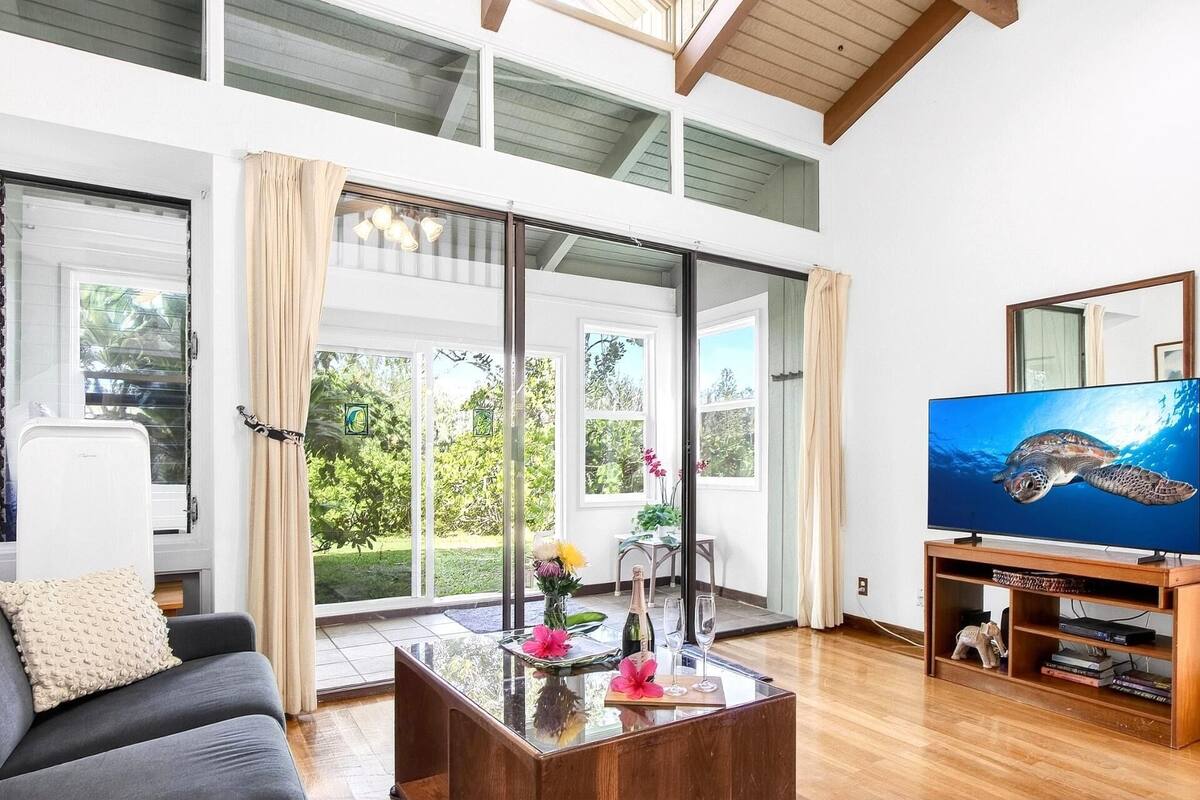 A spacious living room with large windows, a flat-screen TV, and a wooden coffee table.