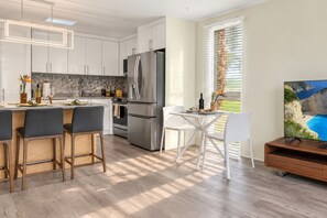 A modern kitchen with white cabinets, stainless steel appliances, and a dining area with a white table and chairs. - Kuilima Estates Resort by KBM (Kahuku)