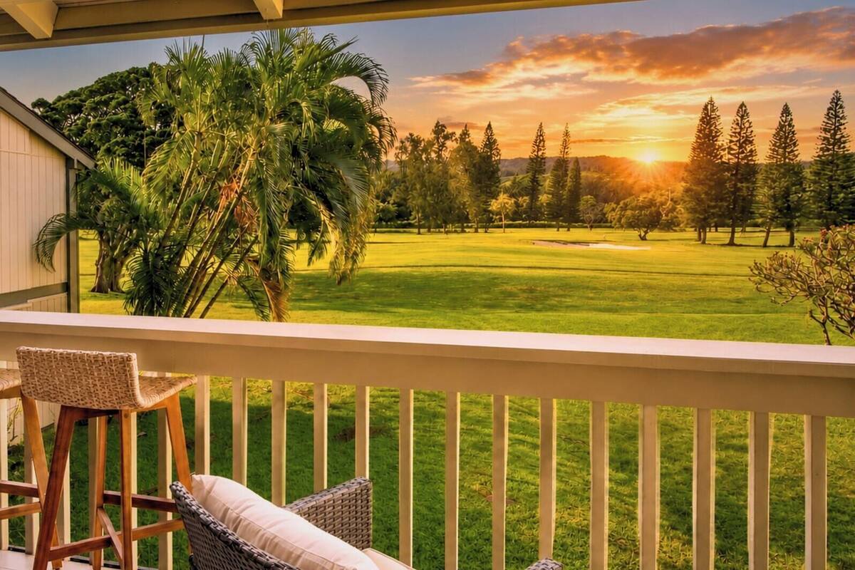 A balcony with wicker furniture, overlooking a golf course with trees and a sunset.