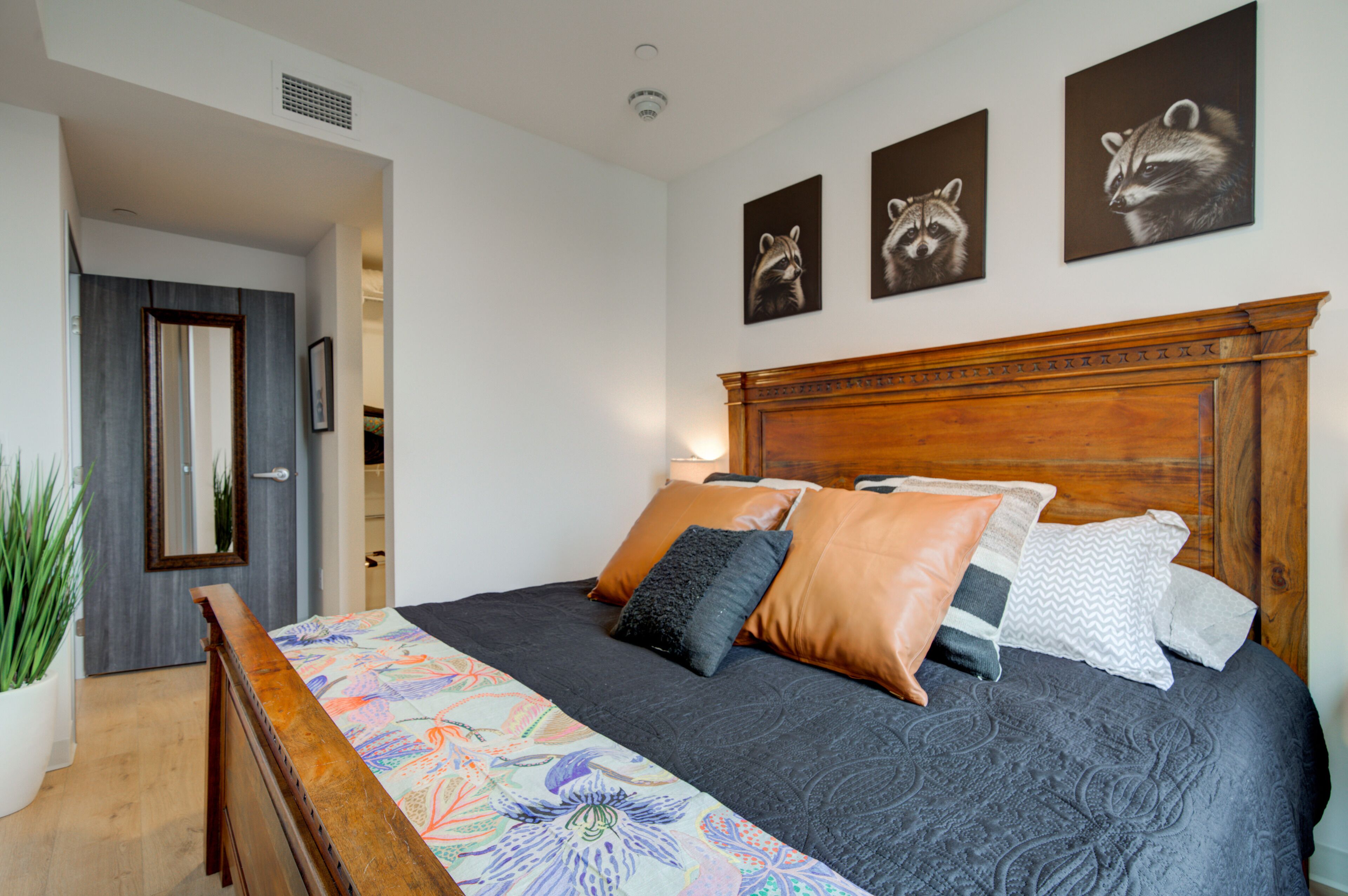 Een slaapkamer met een houten hoofdbord, een bed met meerdere kussens, een kleurrijke sprei en drie kunstwerken met eekhoornmotieven.