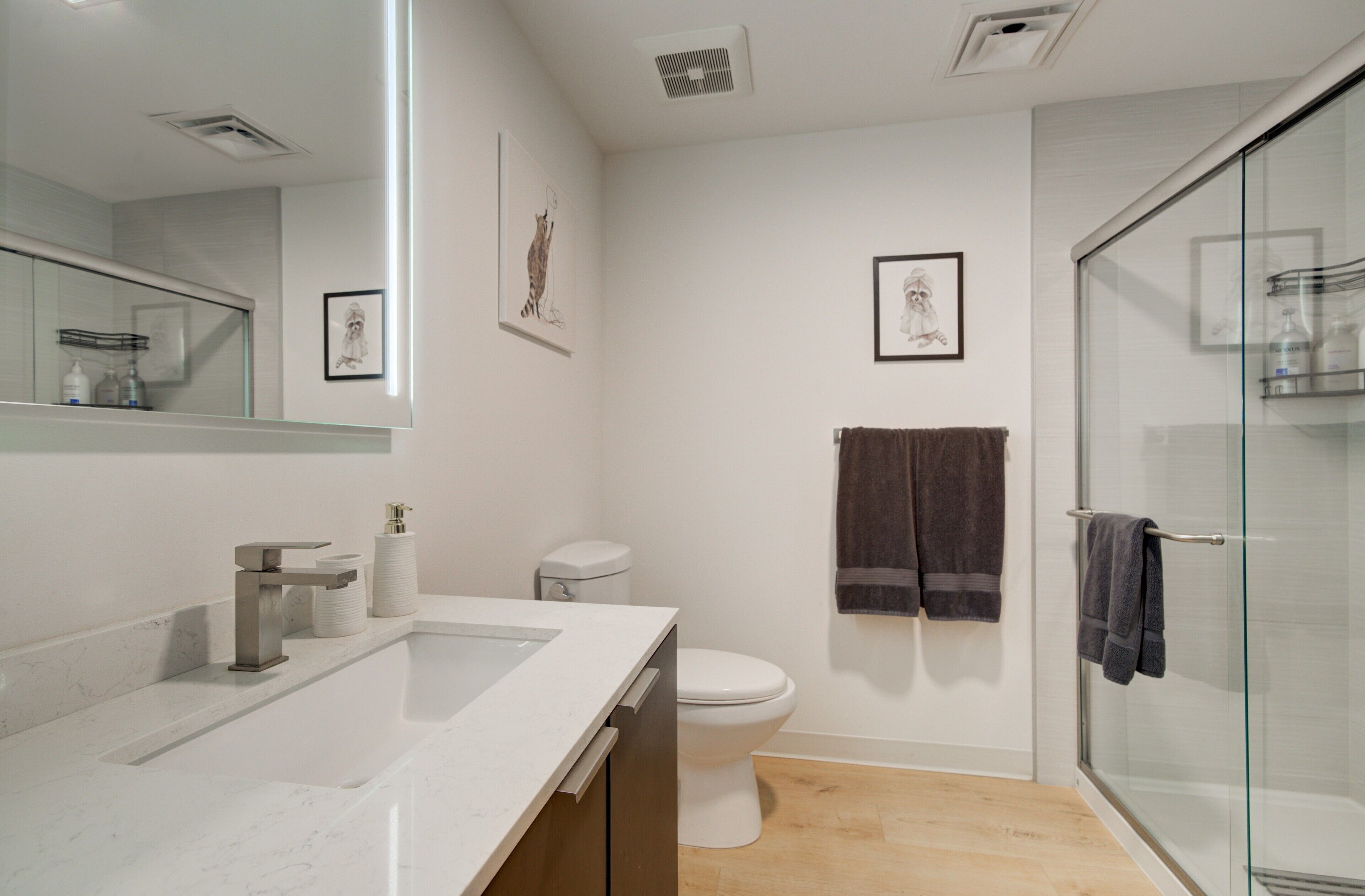 A modern bathroom with a white sink, toilet, and glass shower enclosure.