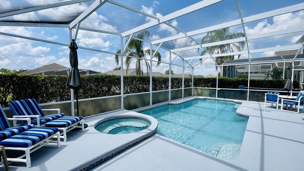 A covered outdoor swimming pool with lounge chairs and a hot tub.