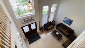 A spacious living room with a high ceiling, large windows, and a staircase leading to an upper floor.