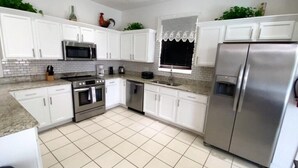 A modern kitchen with white cabinets, stainless steel appliances, and a tiled floor.