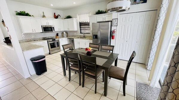 A modern kitchen with white cabinets, stainless steel appliances, and a dining area with a table and chairs.