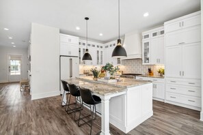 A modern kitchen with white cabinets, a granite countertop, and black pendant lights.
