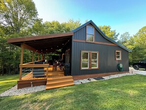 A modern cabin with a covered deck, large windows, and a garage. - Cabin in Hocking Hills with Hot Tub, Fire Pit and Covered Back Deck. (South Bloomingville)