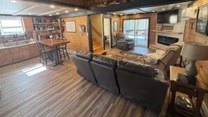 A spacious living area with a fireplace, a dining area with a wooden table and chairs, and a cozy seating area with a sofa and armchairs. - Cabin in Hocking Hills with Hot Tub, Fire Pit and Covered Back Deck. (South Bloomingville)